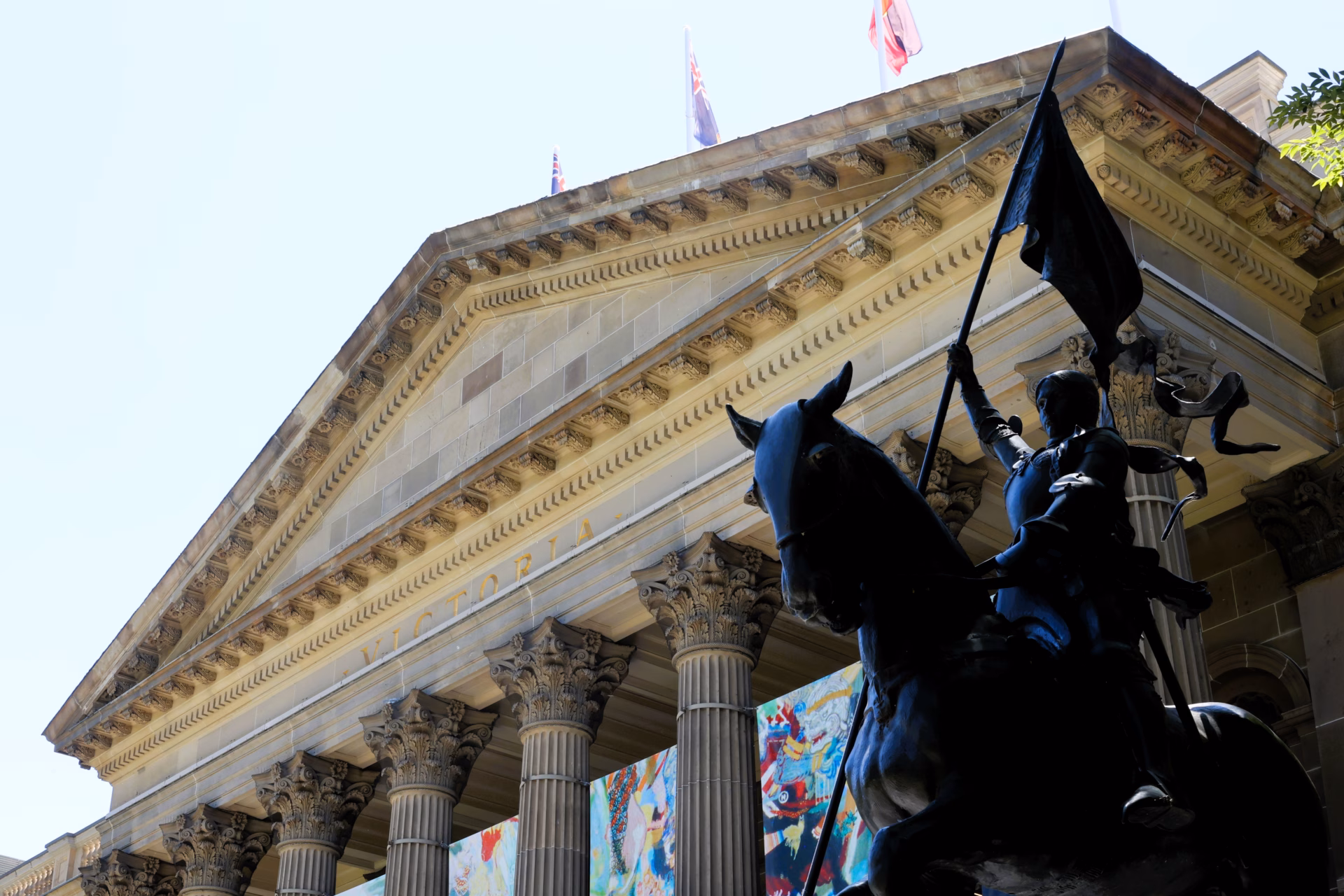 State Library Victoria Melbourne exterior facade with neoclassical columns Victoria inscription and Joan of Arc equestrian statue in foreground