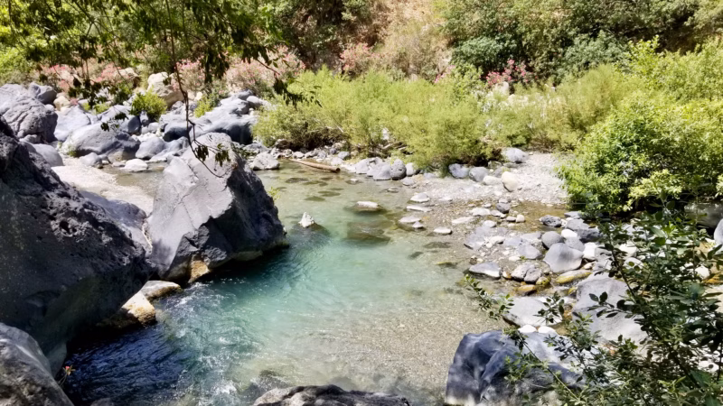 Alcantara Gorges Sicily turquoise river flowing between dark basalt boulders with pink oleander and green vegetation