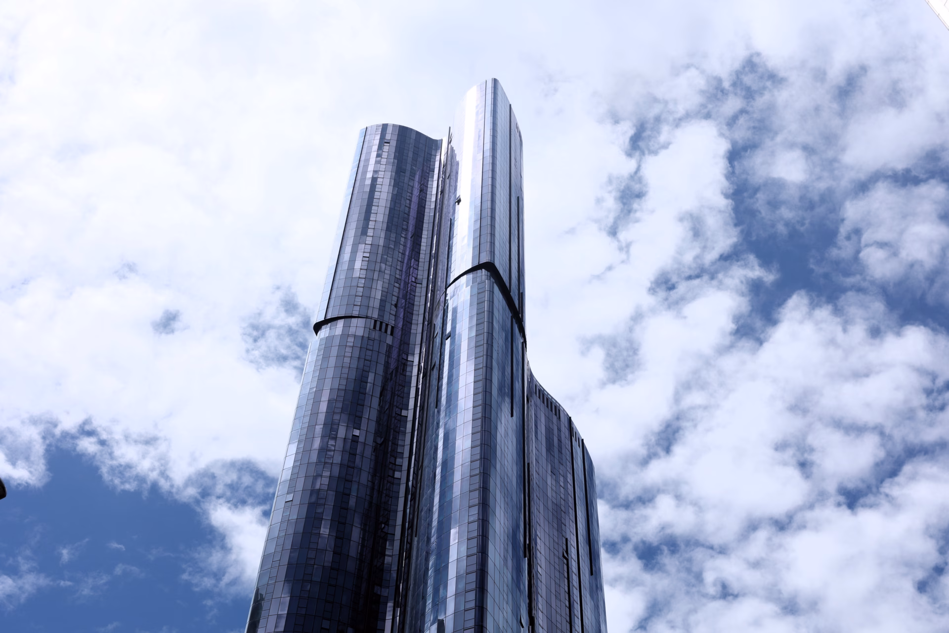 Looking straight up at the Ritz-Carlton Melbourne twin glass skyscraper towers against blue sky and clouds