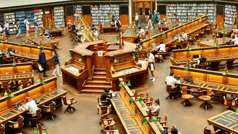 Overhead view of the La Trobe Reading Room at State Library Victoria Melbourne showing circular wooden reading desks with green lamps.