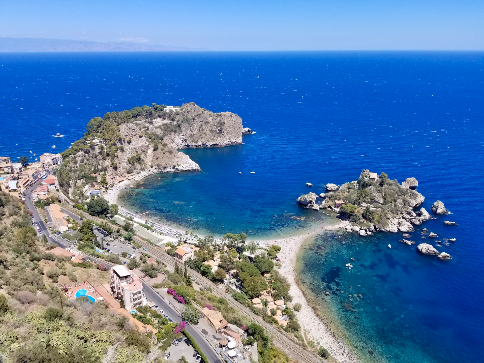 Aerial view of Isola Bella Taormina Sicily with turquoise water curved beach and rocky island connected by sandy path