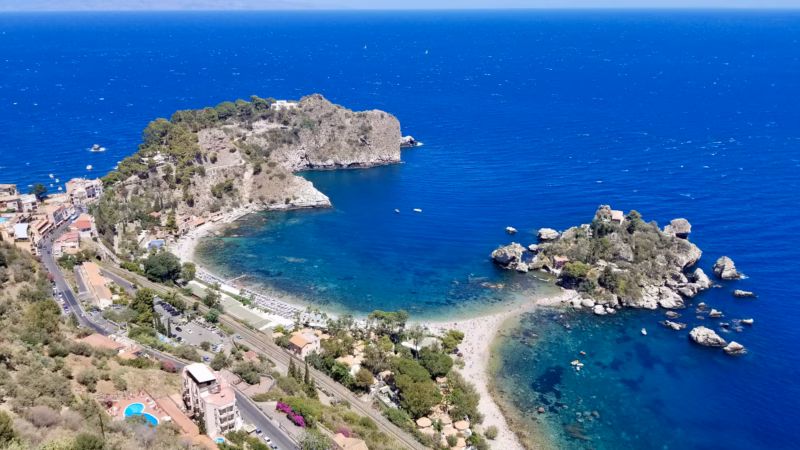 Aerial view of Isola Bella Taormina Sicily with turquoise water curved beach and rocky island connected by sandy path