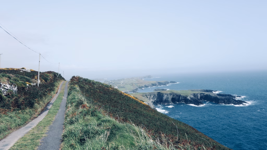 Narrow cliff road running along the Brow Head headland edge with the Atlantic to the right and gorse slopes left