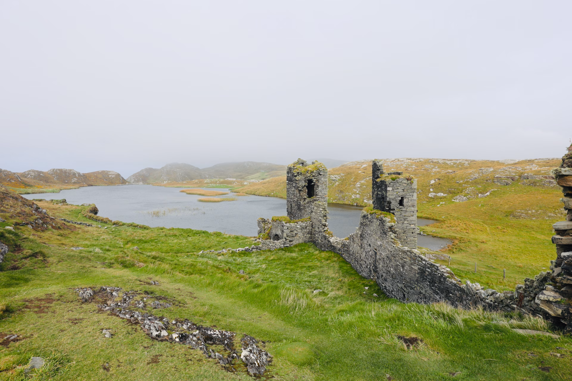 Two ruined towers of Dunlough Castle with Lough Fadda stretching behind, mist covering the hills of the Mizen Peninsula