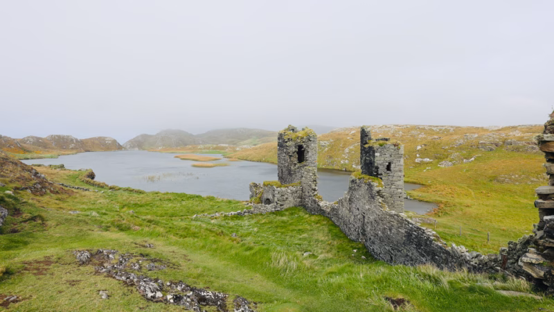 Two ruined towers of Dunlough Castle with Lough Fadda stretching behind, mist covering the hills of the Mizen Peninsula