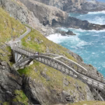 Mizen Head Bridge spanning the gorge from above with people crossing and turquoise Atlantic below