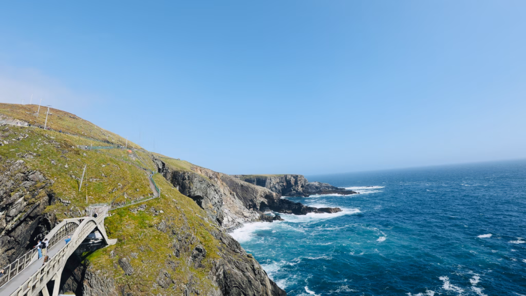 View from on top of the Mizen Head Bridge looking back toward the mainland cliff and coast, blue sky above