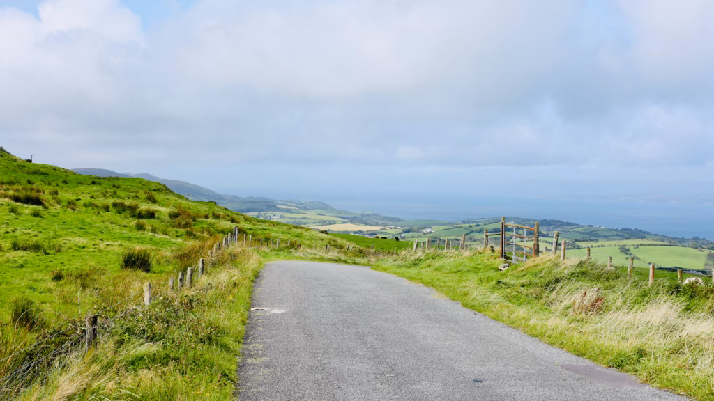 Narrow West Cork road descending toward the Atlantic from Seskin, green hills either side, ocean in distance