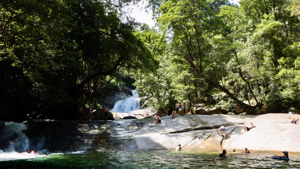 Visitors swimming, sliding, and sunbathing on granite boulders at the main pool of Babinda Boulders