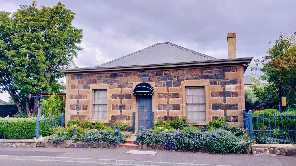 Coursed stone cottage in Battery Point with a navy awning and iron fence covered in purple flowers