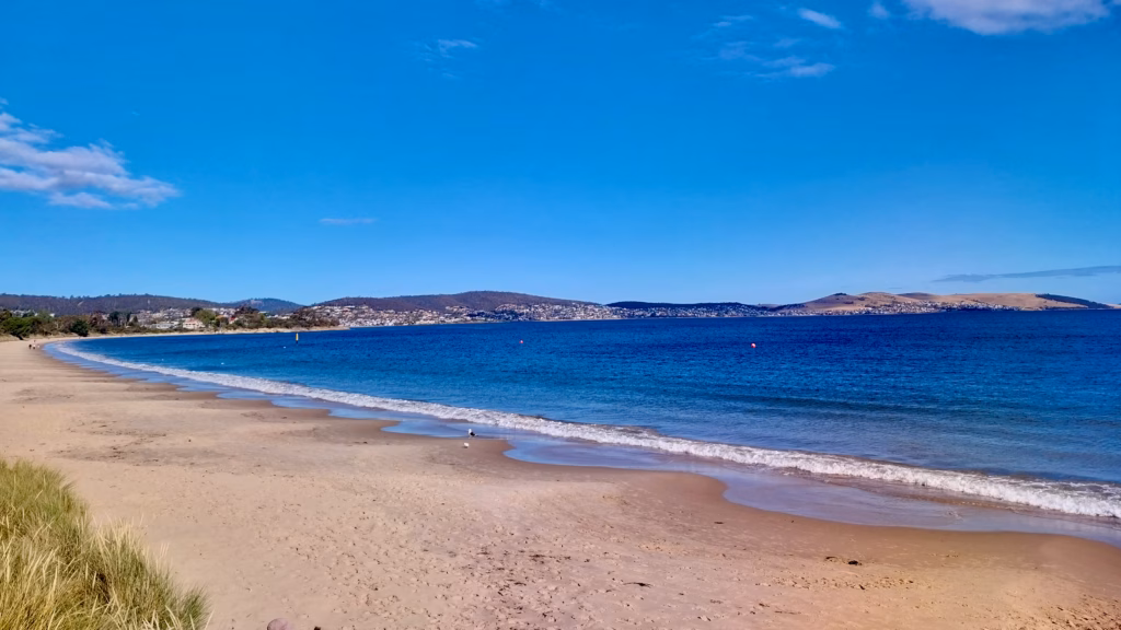 Wide curve of Bellerive Beach with the Derwent River and distant hills at afternoon