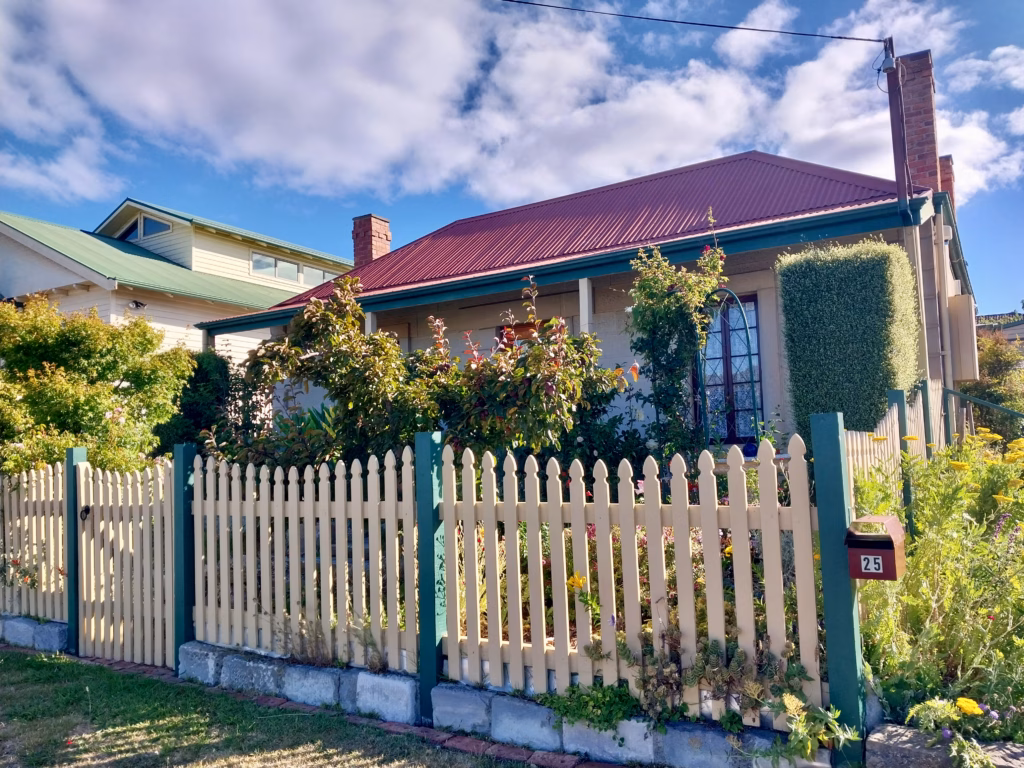 Weatherboard heritage cottage in Bellerive with red roof, teal-and-cream picket fence and cottage garden