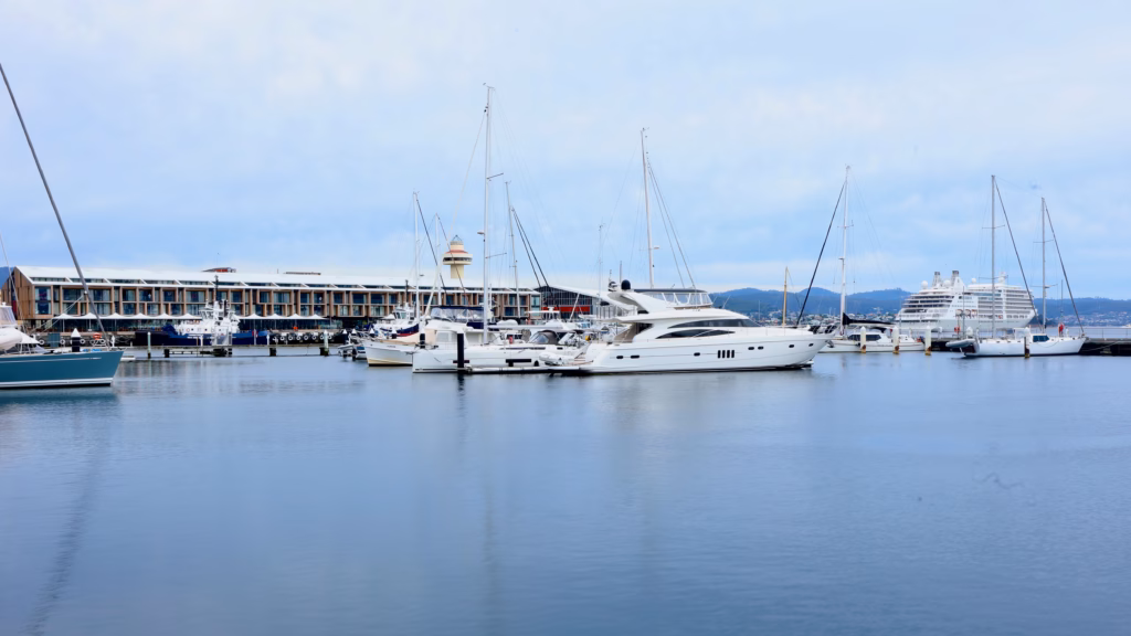 Marina at Hobart waterfront with sailing boats, a luxury motor yacht, and a cruise ship in the background