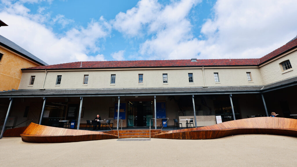 TMAG heritage courtyard with sandstone buildings and a wave-shaped timber bench