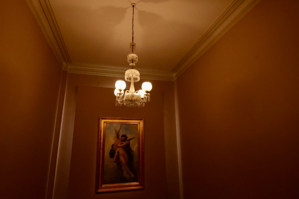 Antique crystal chandelier and gilt-framed painting in a dim TMAG hallway
