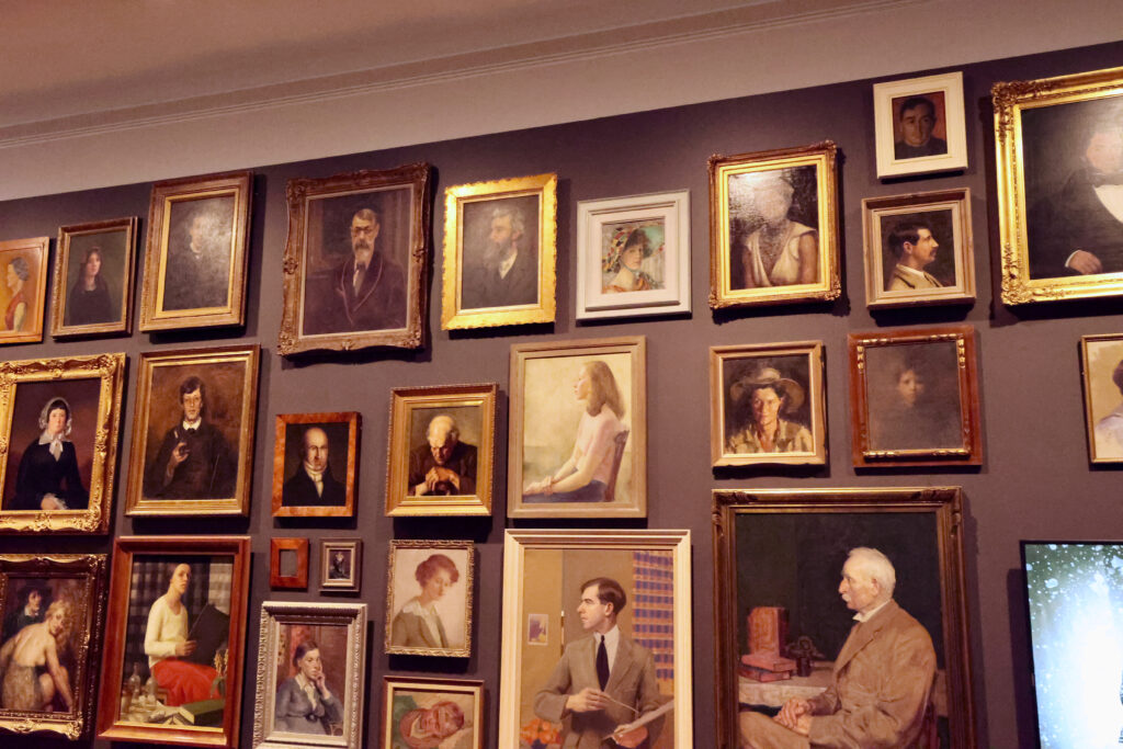 Dense salon-style wall of framed portrait paintings at TMAG