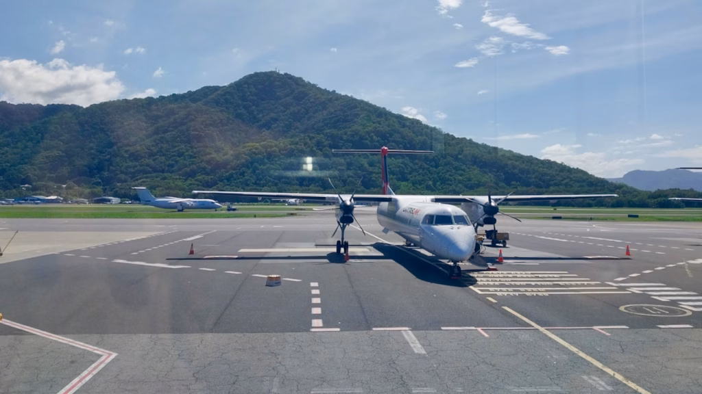 A regional Dash-8 aircraft on the tarmac at Cairns Airport with the ranges behind it