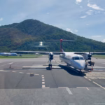 A regional Dash-8 aircraft on the tarmac at Cairns Airport with the ranges behind it