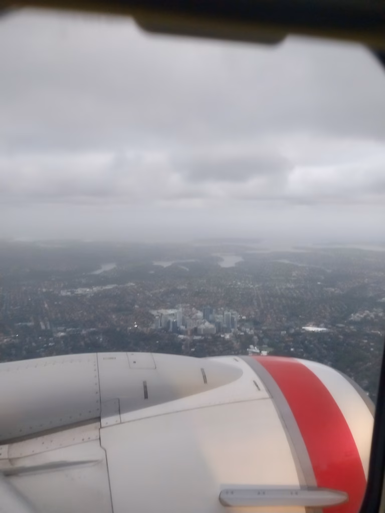 Sydney Harbour Bridge and Opera House visible through cloud during a rainy descent into Sydney