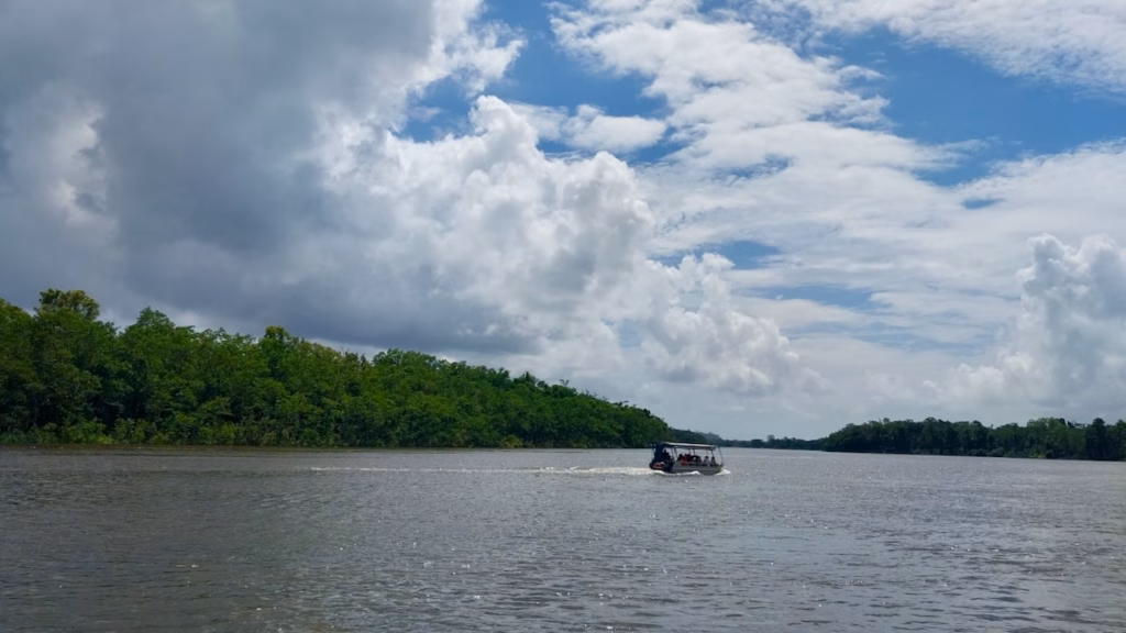Small tour boat crossing the wide Daintree River under a heavy, cloud-filled sky
