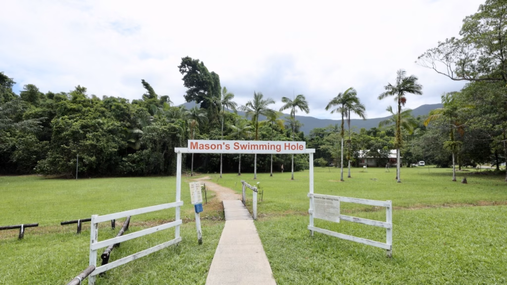 Entrance sign for Mason's Swimming Hole, with palm trees and mountains behind