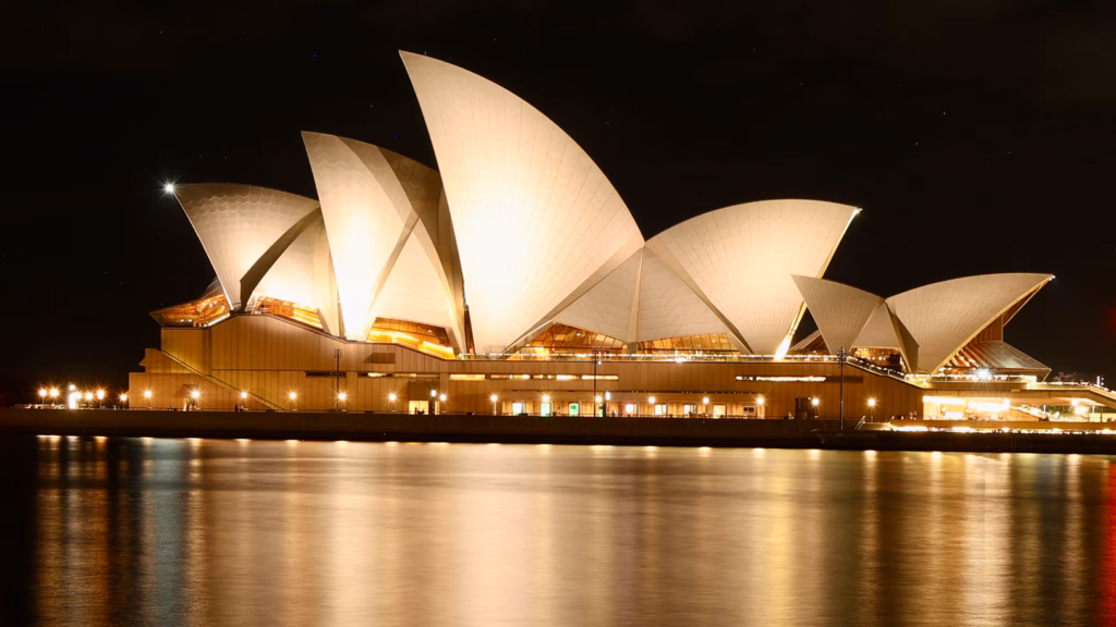 Sydney Opera House sails illuminated at night, reflected in the harbour