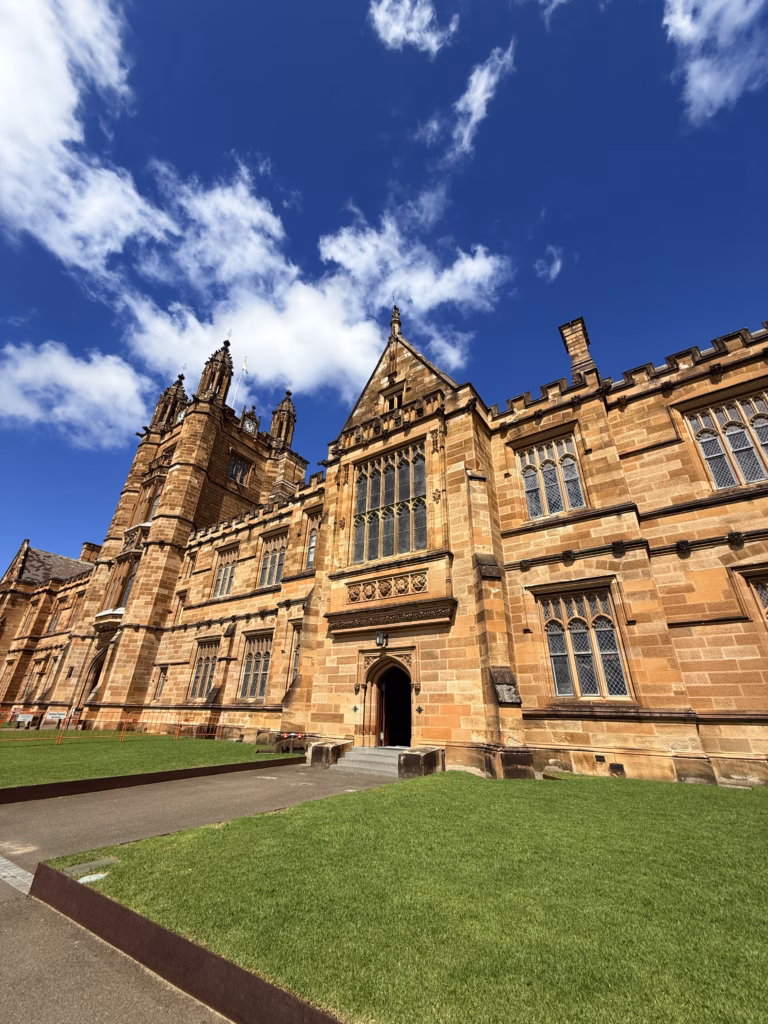 The University of Sydney's sandstone Main Quadrangle building under a blue sky