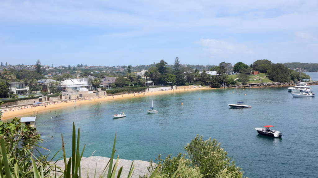 Crowded Camp Cove beach at Watsons Bay seen from above, with moored boats and the grassy Green Point headland