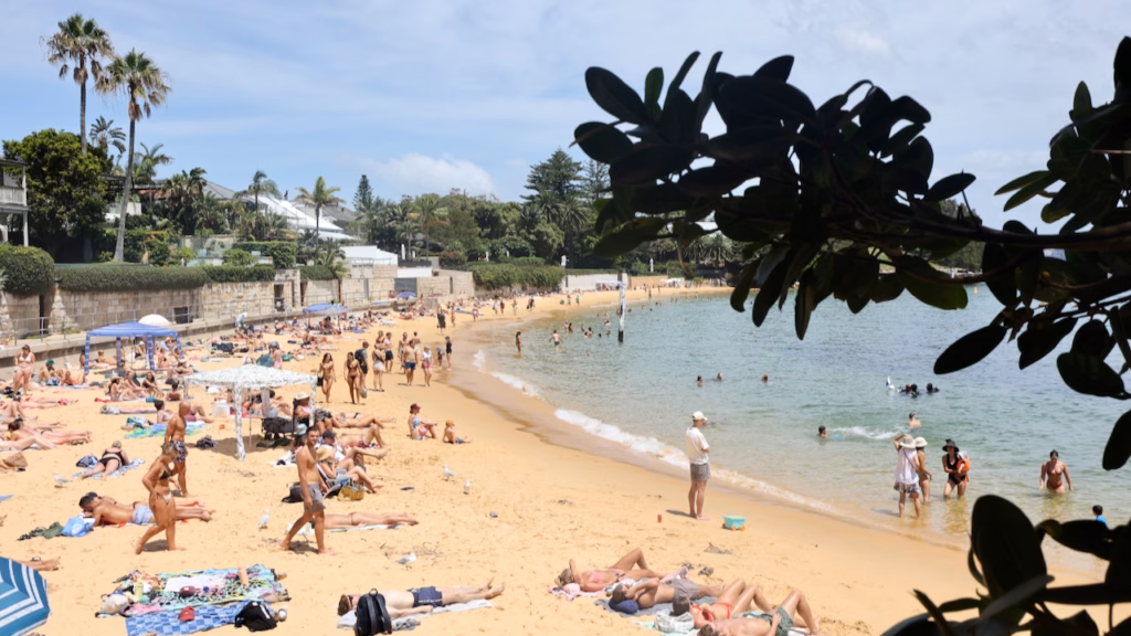 Crowded Camp Cove Beach at Watsons Bay with swimmers in calm harbour water and sunbathers on the sand