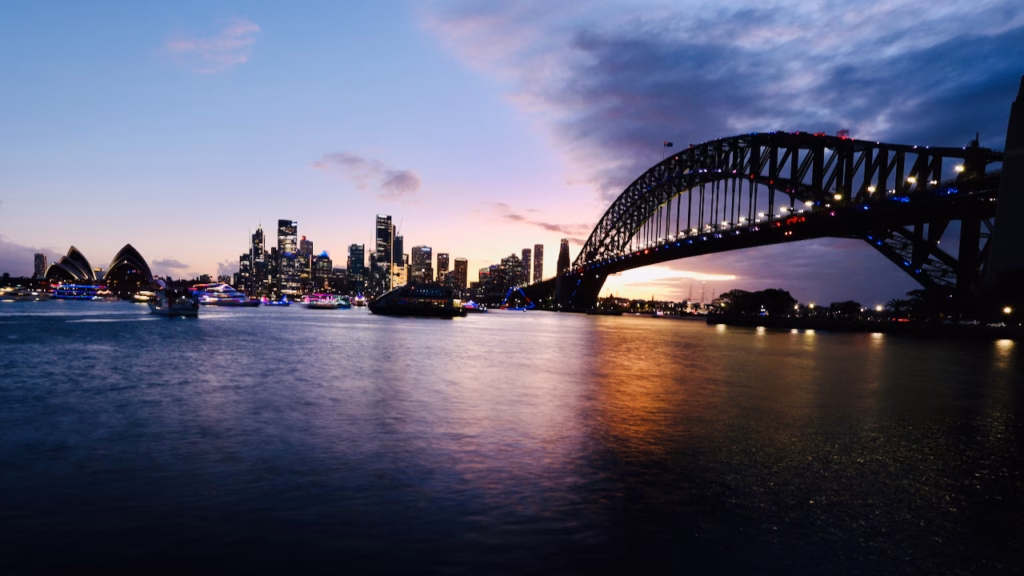 Sydney Opera House, skyline and Harbour Bridge at dusk with numerous illuminated decorative boats gathered on the water ahead of a fireworks display