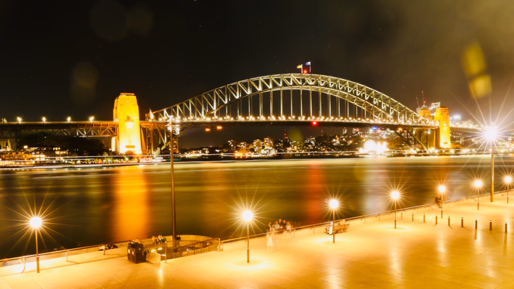Sydney Harbour Bridge at night, long exposure, viewed from the Sydney Opera House's Monumental Steps, Luna Park's lit ferris wheel visible near the bridge's base