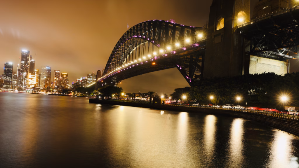 Sydney Harbour Bridge and CBD skyline at night, viewed while walking back from Kirribilli toward Circular Quay, a road with parked cars along the water