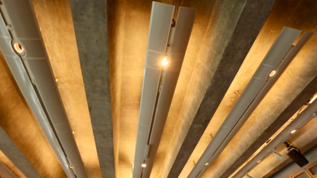 Close upward view of illuminated vertical panels mounted on the Sydney Opera House's angled interior ceiling, warm lighting, track lights visible