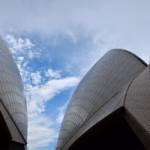 Sydney Opera House sail shells seen from between two adjoining shells against a bright blue sky with scattered clouds, taken during the guided tour