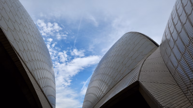 Sydney Opera House sail shells seen from between two adjoining shells against a bright blue sky with scattered clouds, taken during the guided tour