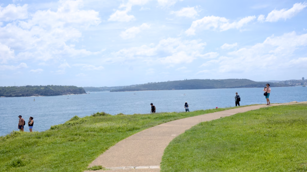 Paved path across a grassy headland on the South Head Heritage Trail at Watsons Bay, with walkers and views across Sydney Harbour
