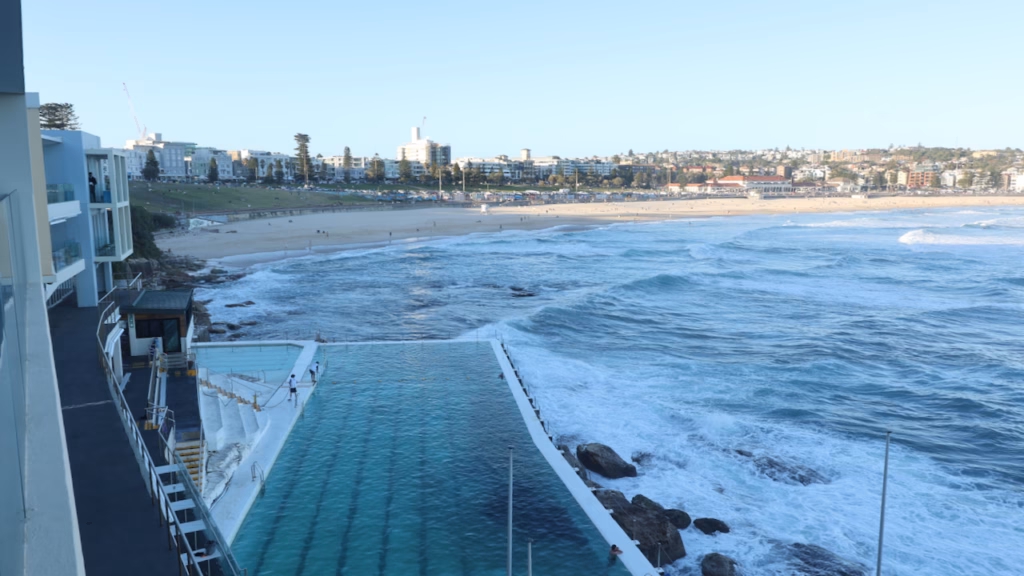 A swimmer dives into the Bondi Icebergs pool as waves break over the outer wall