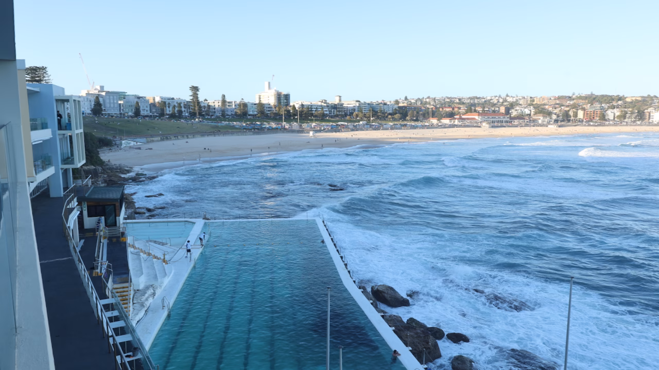 A swimmer dives into the Bondi Icebergs pool as waves break over the outer wall