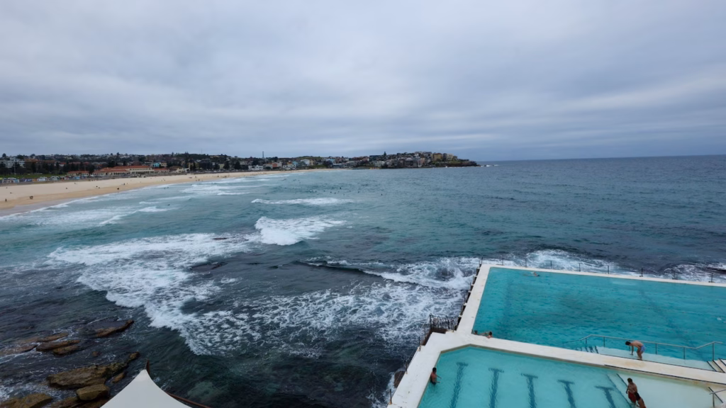 The Bondi Icebergs main pool and children's pool seen from above, with waves breaking on the rocks and Bondi Beach beyond