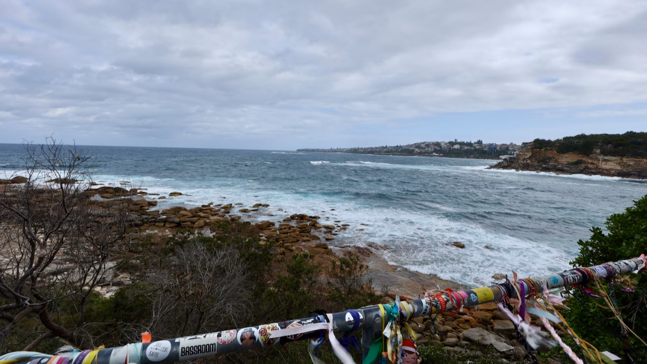A railing covered in stickers, festival wristbands and ribbons on the Coogee to Bondi walk