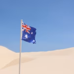 Australian flag flying on a bare sand dune under a blue sky at the Stockton dunes, Port Stephens
