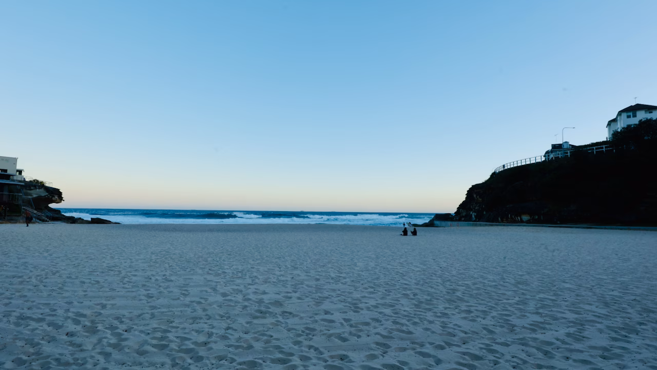 Tamarama Beach at dusk with a few people on the sand