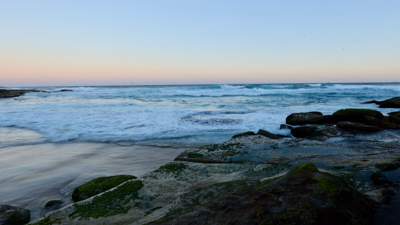 Long exposure of waves over rocks at Tamarama under a pink evening sky